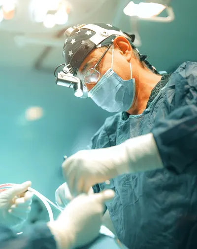 Surgeon wearing a surgical cap, mask, and magnifying glasses, performing surgery in an operating room