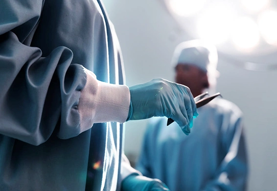Close-up of a surgeon in scrubs and gloves holding a surgical instrument, with another medical professional in the background, in an operating room