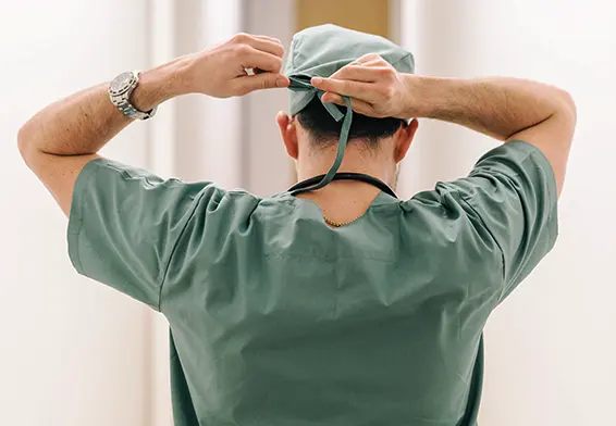 A surgeon in green scrubs tying their surgical cap before entering the operating room