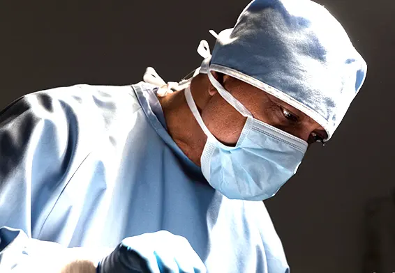 Surgeon wearing a blue surgical gown, mask, and cap, focused on performing surgery